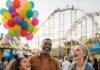 Top 10 Family-Friendly Travel Destinations for 2025 Laughing family at theme park with roller coaster and balloons.