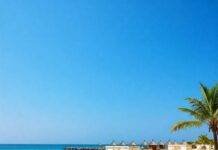 Dreamy Beach Resorts You Can’t Miss This Summer Wide-angle beach with resort cabanas and azure water.