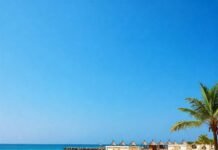 Dreamy Beach Resorts You Can’t Miss This Summer Wide-angle beach with resort cabanas and azure water.